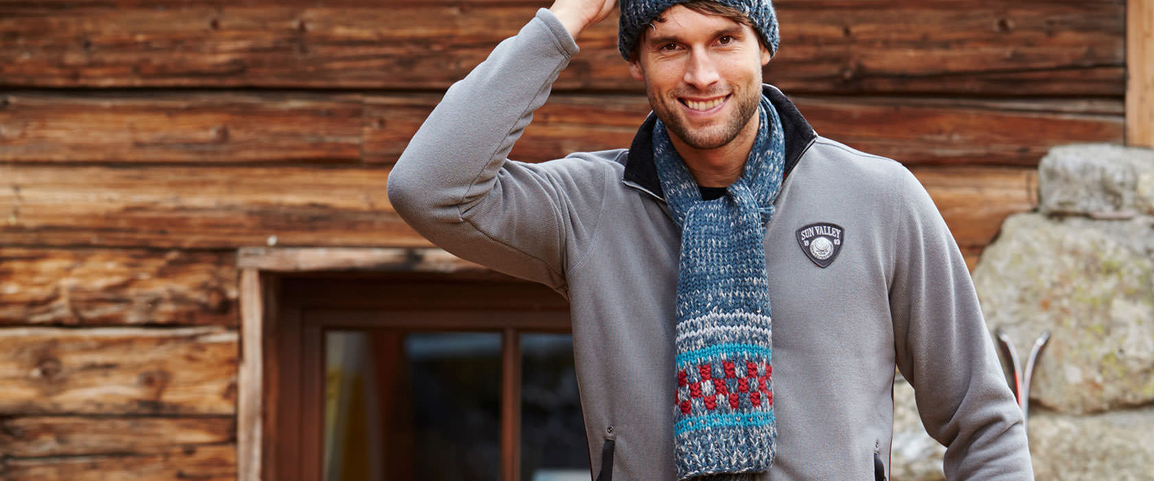 A man wearing a ski fleece in front of a chalet 