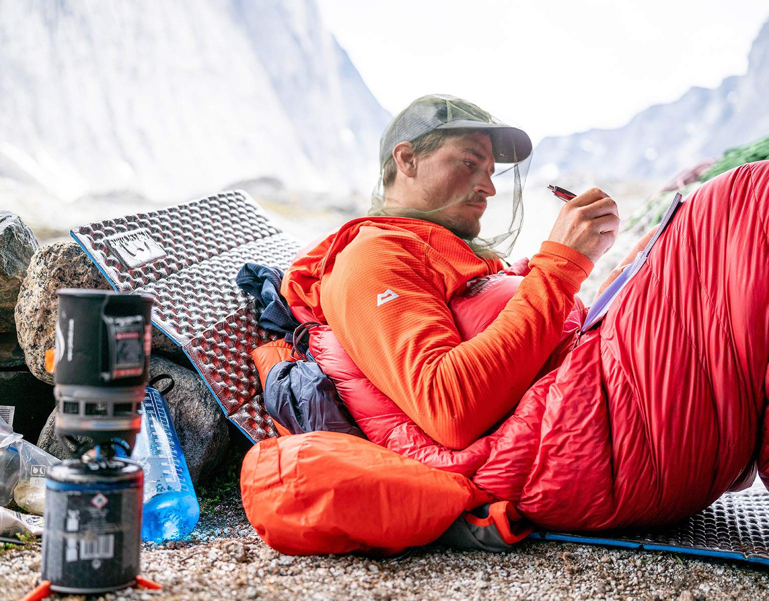 man making notes in notebook surrounded by mountain equipment