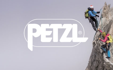 Two people are almost at the top of a rock, wearing and using Petzl gear.