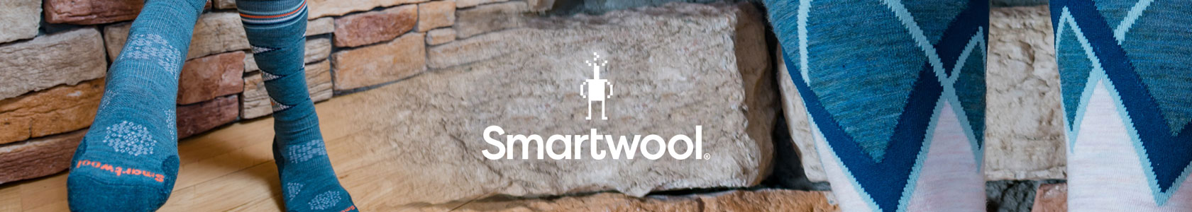 Person's feet by a stone wall, wearing Smartwool socks