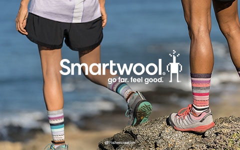 Person's feet by a stone wall, wearing blue Smartwool socks