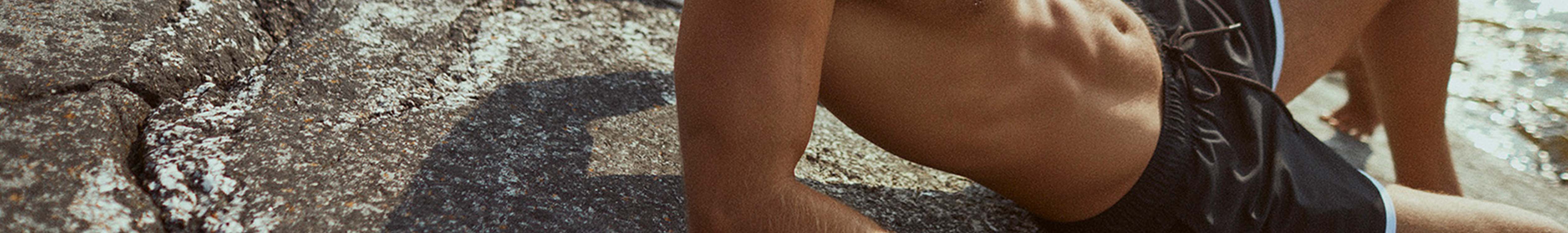 A man is sunbathing next to the sea, wearing Bjorn Borg swimming shorts.