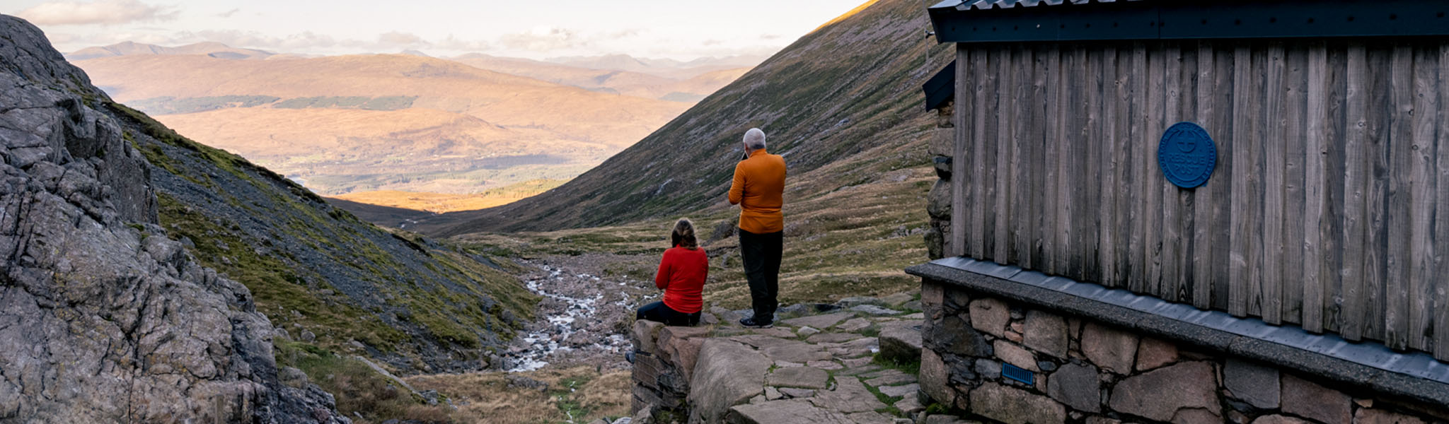 Two people are with their backs to cameras, looking at the beautiful nature and enjoying a cup of tea.