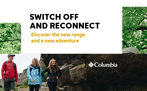 Two people are standing by a lake during falling snow, wearing Columbia clothing.