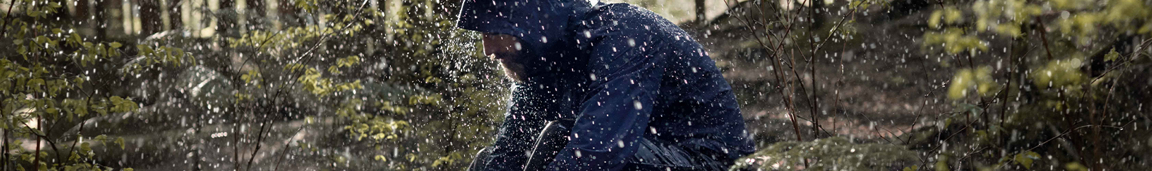 A man is sitting on a fallen tree under rain, wearing gear with GORE-TEX.