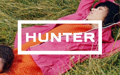 Two women laying down on a grass, wearing Hunter pink jackets and Hunter wellies