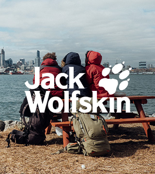 Three people sitting on a bench in Jack Wolfskin gear and enjoying the river view next to a city