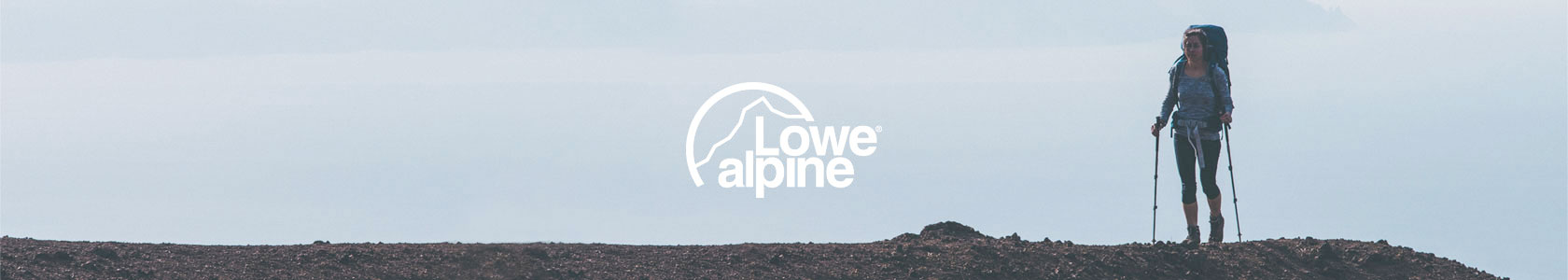 A woman stood at the top of a hill, wearing a Lowe Alpine backpack and holding walking sticks