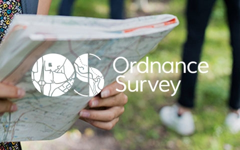 A woman is outdoors, holding and looking at an Ordnance Survey map