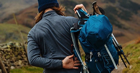A man walking away from the camera somewhere in the countryside and putting his rucksack on.