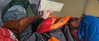 Man in sleeping bag and tent reading map