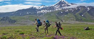 Three hikers walking across a filed with a mountain range in the background