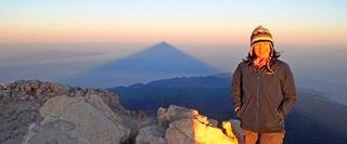 Woman smiling whilst standing on top of a mountain at sunrise