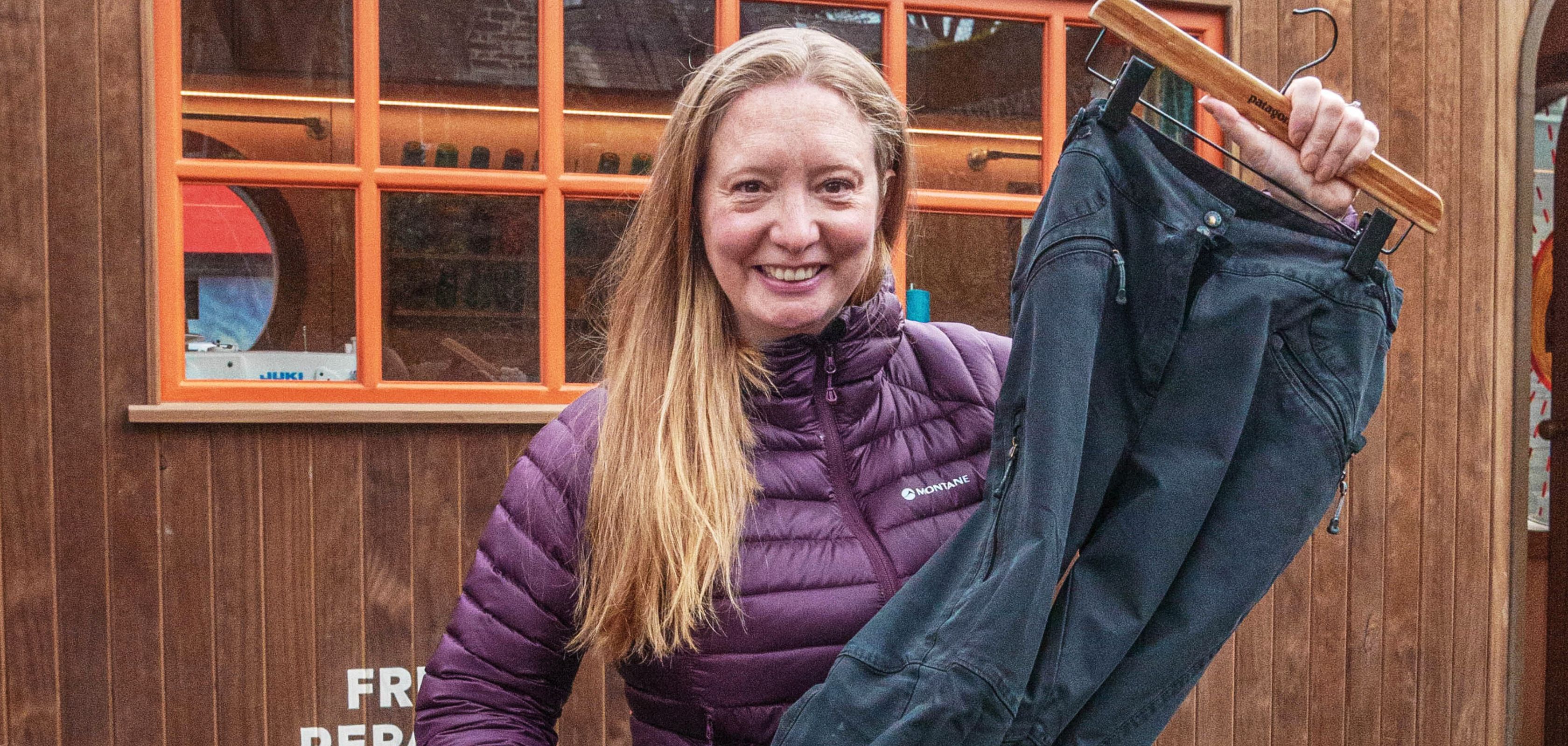 A bblonde woman in a purple coat holding a pair of trousers
