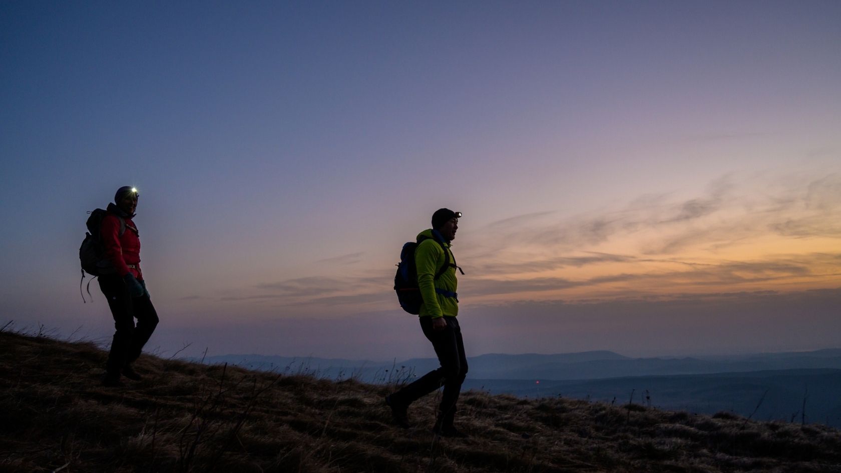 Two hikers walking at night with head torches