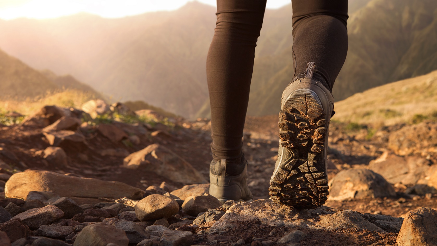 Someone walking away from camera in sunset lighting with their boot on. You can see the tread.