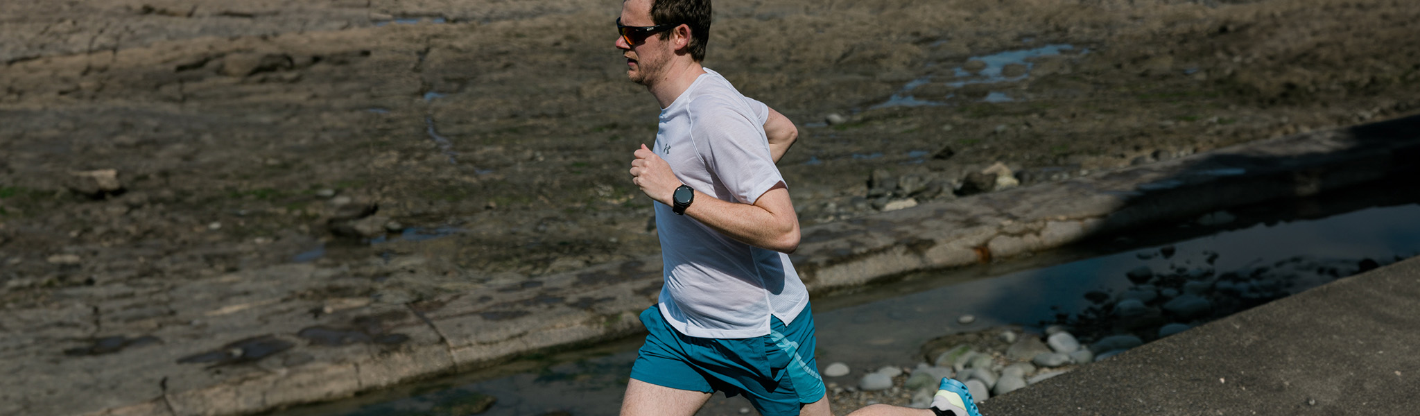 A man is running on a trail, wearing a white t-shirt and blue shorts