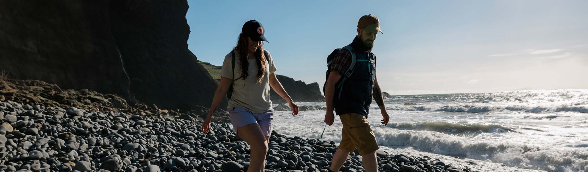 Two people are walking on a pebble beach