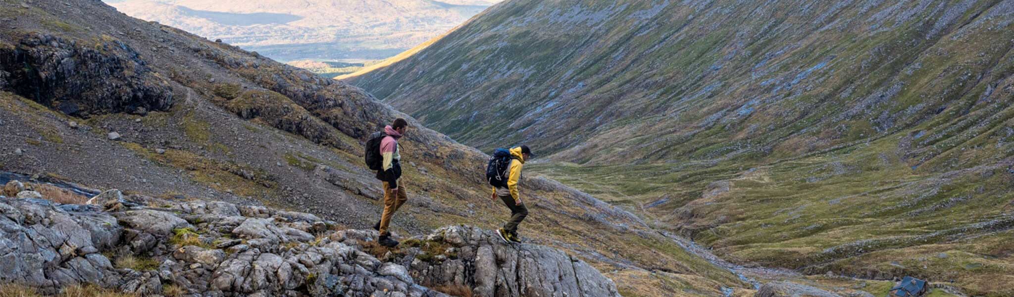 Two people are hiking donw a hill, wearing walking kit and backpacks