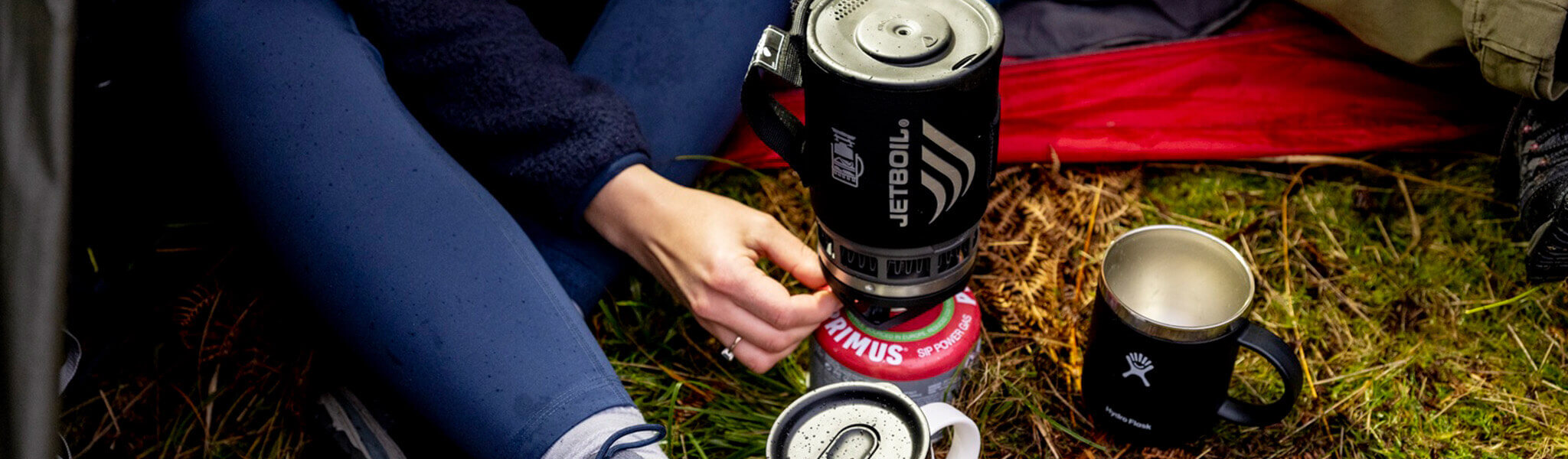 Travel mugs and Jetboil with Primus system to boil water outdoors with person's feet next to them