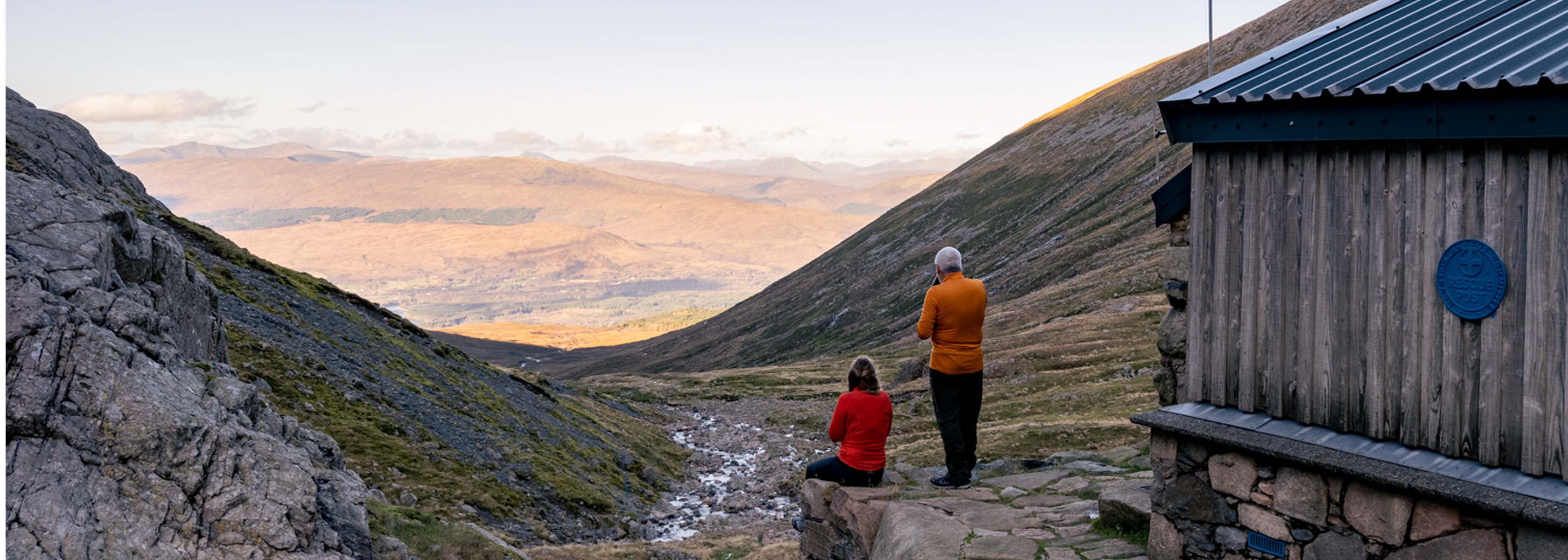 Two people are with their backs to cameras, looking at the beautiful nature and enjoying a cup of tea.