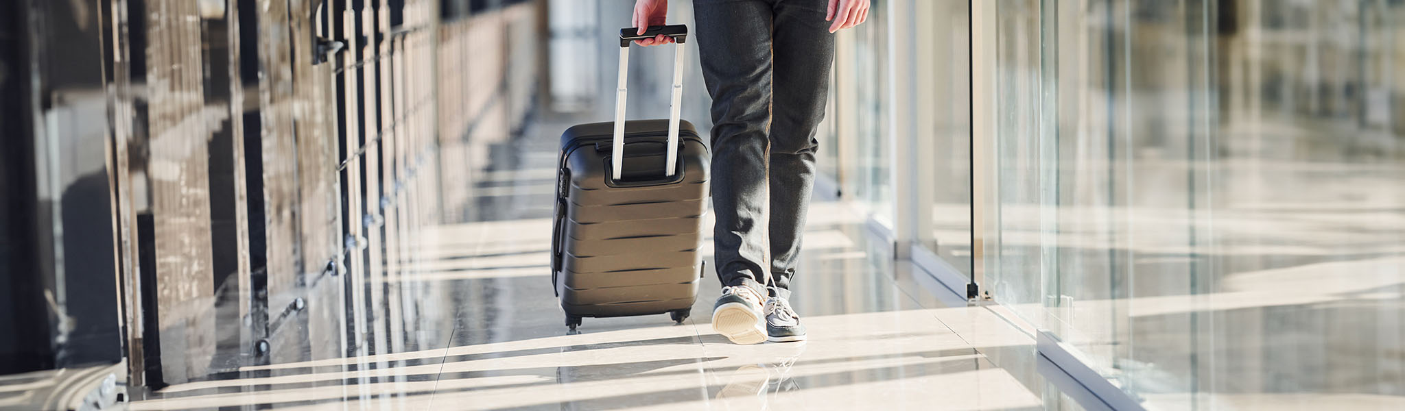 A person's lowest half of the body is walking in an airport with a wheelie bag.