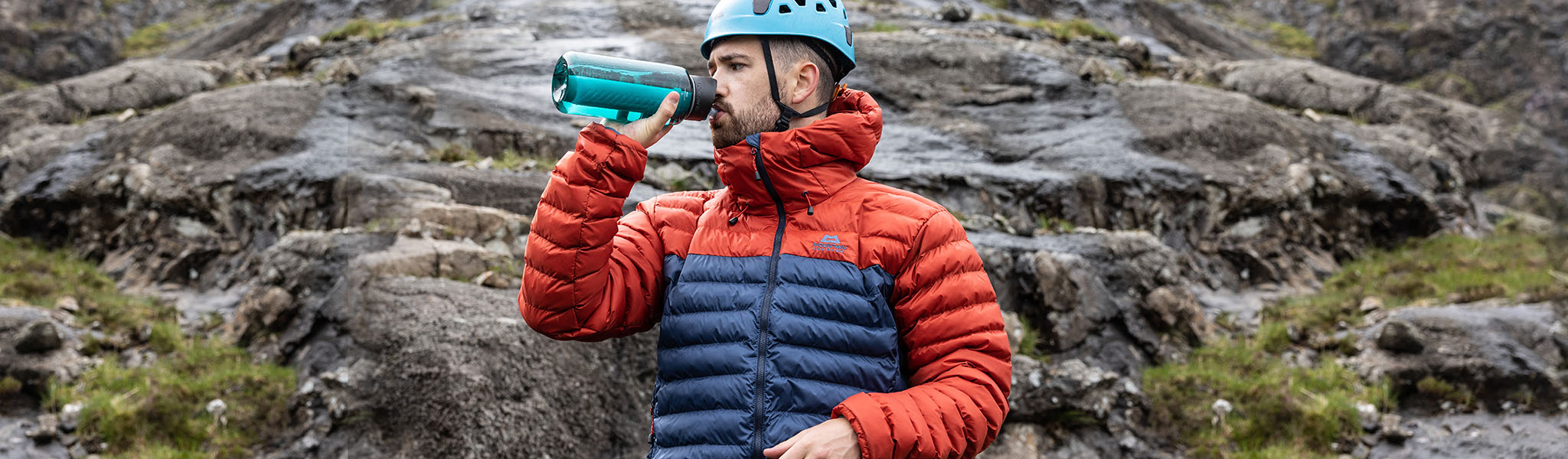 A man wearing an insulated jacket next to a rocky cliff 