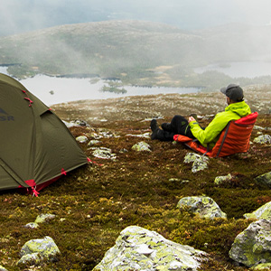 Man on camp chair with tent in the wilderness