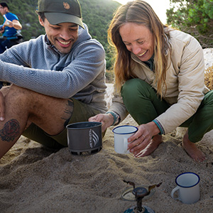 A mana and woman on the beach making a hot drink with camping stove