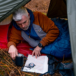 Man in tent with sleeping bag, map and travel mug