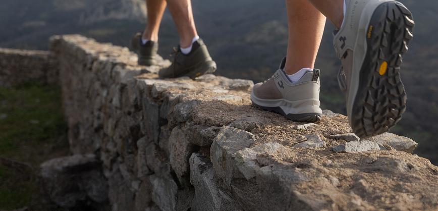 Two Women walking ontop of small wall in the nature wearing walking shoes and shorts