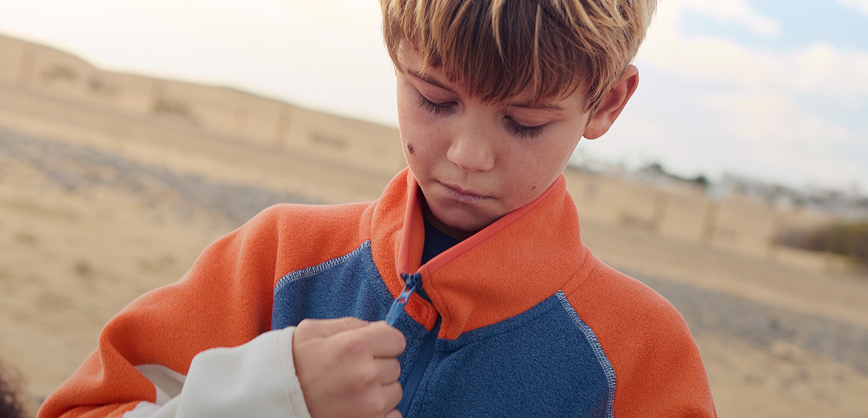 Boy wearing a blue and orange fleece near the beach