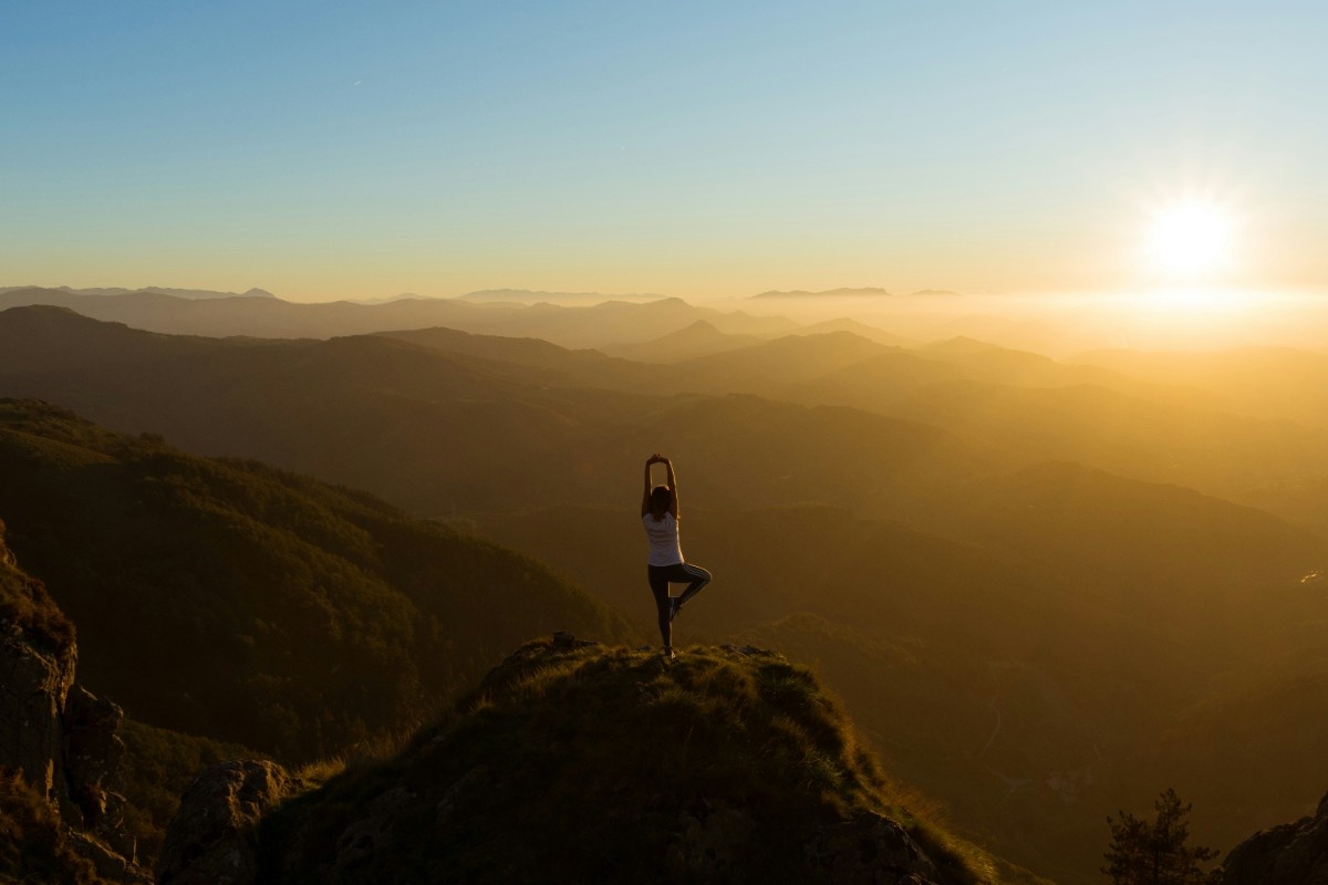 A person doing yoga on a mountain looking out to the sunrise 