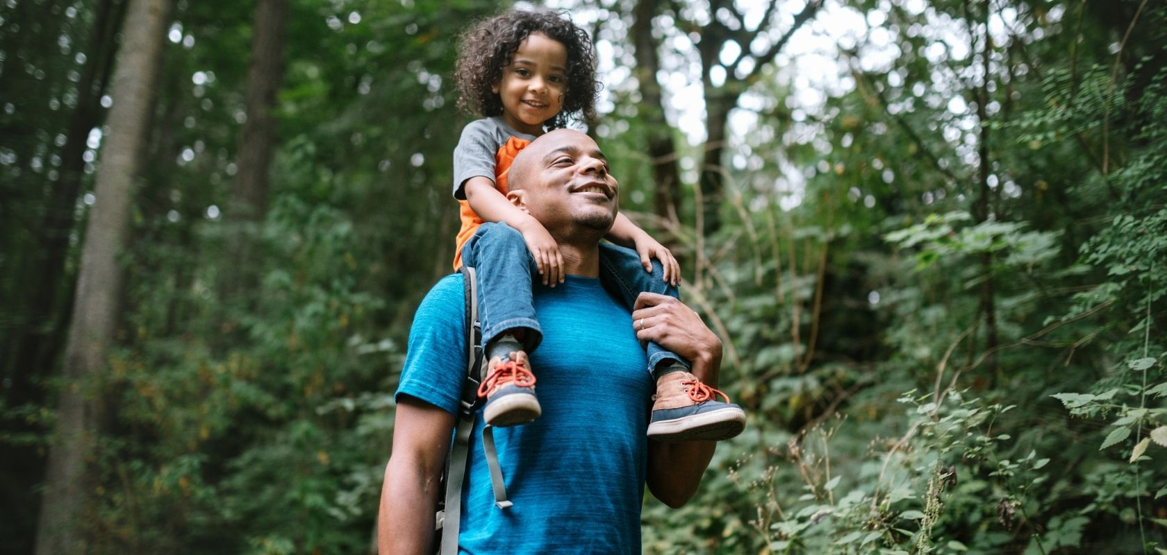 A man carrying his child on his shoulders through the woods 