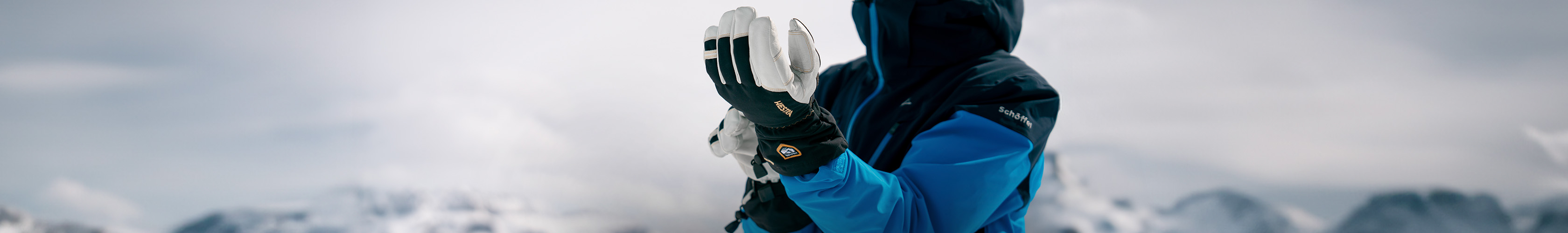 Shop Snow + Rock new season accessories. A man is adjusting his ski glowes