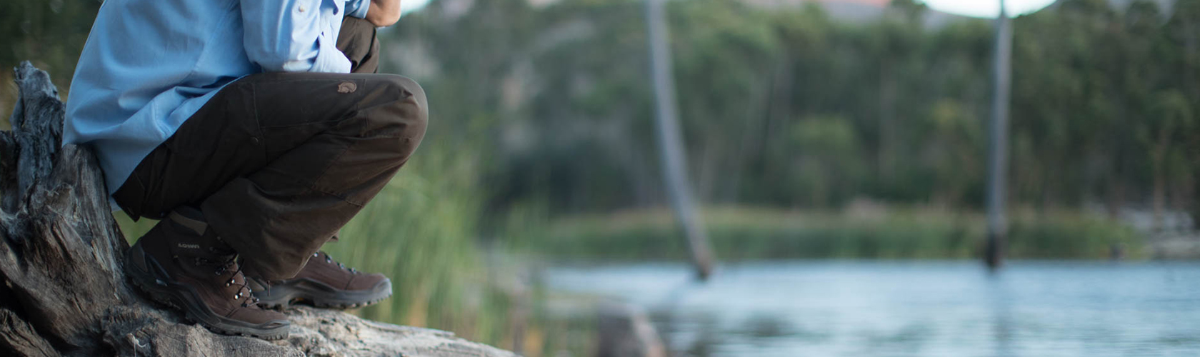 An image of a man crouched by a lake in walking trousers 